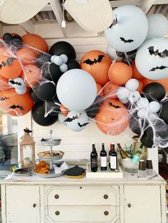 an assortment of halloween balloons hanging from the ceiling in front of a buffet table with wine bottles