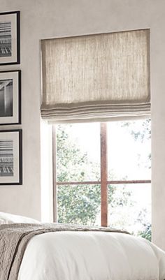 a bed sitting under a window next to pictures on the wall and below it is a white bedspread