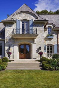 a large stone house with blue shutters on the front door and windows, surrounded by greenery