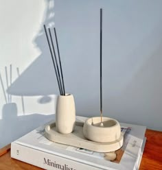 two white vases with sticks sticking out of them on top of a bookshelf