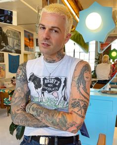 a man with tattoos standing in front of a store counter and looking at the camera