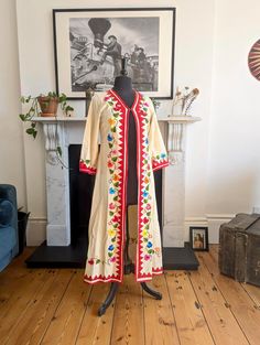 Discover a piece of history with this exquisite Vintage 1970's Mexican Hand Embroidered Linen Jacket Robe. Unique and timeless, this robe is a testament to the intricate craftsmanship and vibrant style of the 70's era Era: 1970's Material: high-quality linen Design: Hand embroidered floral patterns on the front, hem, and cuffs Closure: Single eyelet at the top Size: Small (UK 8) Pit to pit 41cm Sleeve length 46cm Shoulder Width 36cm Full length 120cm Waist 46cm Condition: excellent vintage condi Vintage Long Embroidered Outerwear, Vintage Cream Outerwear With Floral Embroidery, Festive Vintage Embroidered Kaftan, Vintage Long Sleeve Kimono For Festival, Vintage Long Fitted Robe, Vintage Embroidered Long Sleeve Kaftan, Vintage Embroidered Kaftan For Festival, Vintage Long Sleeve Kimono For Festive Occasions, Vintage Long Sleeve Kaftan For Spring