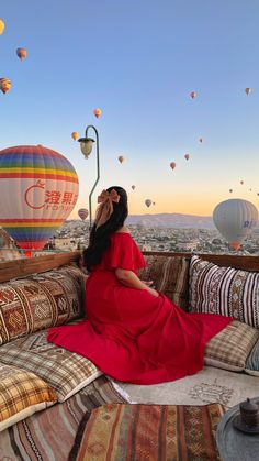 a woman in a red dress sitting on a couch with hot air balloons flying above