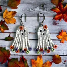 white beaded ghost earrings with orange and purple flowers on them, surrounded by fall leaves