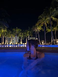 a woman in a swimming pool at night with palm trees and buildings in the background