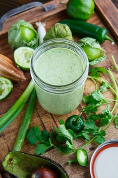 a wooden cutting board topped with green vegetables and a jar of pesto sauce next to it