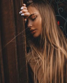 a woman with long blonde hair leaning against a wall and holding her hand on her head