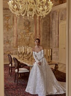 a woman in a wedding dress sitting at a table with chandelier above her