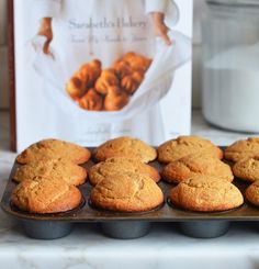 muffins are lined up on a baking tray in front of a cook book