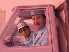 two men sitting in the driver's seat of a pink truck looking at something