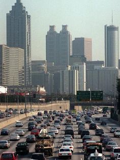 many cars are driving down the highway in front of tall buildings and skyscrapers on either side