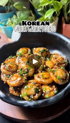 a black bowl filled with cooked shrimp on top of a wooden table next to potted plants