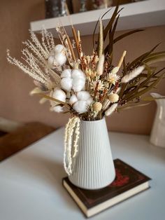 a white vase filled with lots of flowers on top of a table next to a book