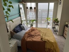 a bed sitting next to a window with lots of plants on top of the bedspread