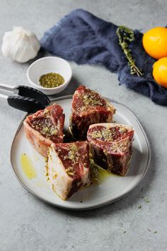 four pieces of meat on a plate next to some oranges and garlic flakes