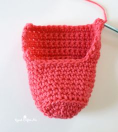 a crocheted red basket hanging from a hook on a white surface with a knitting needle