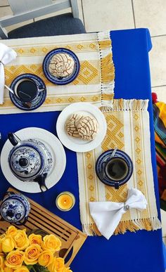 the table is set with blue and white dishes, yellow flowers, and tea cups