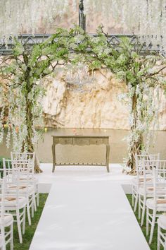 an outdoor ceremony setup with white chairs and greenery on the aisle, decorated with flowers