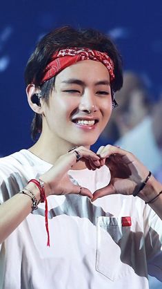 the young man is making a heart shape with his hands while wearing a bandana