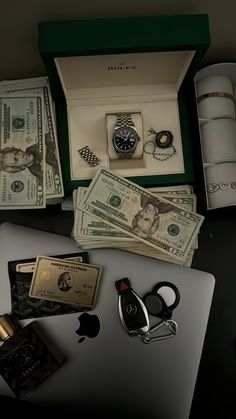 an open box with money, watch and other items on it next to a laptop