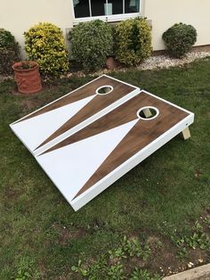 a white and brown cornhole board sitting on top of green grass in front of a house