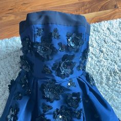 a blue dress with flowers on it is laying on the floor next to a rug