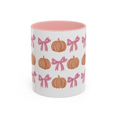 a white and pink mug with pumpkins on the front, bow ties around it