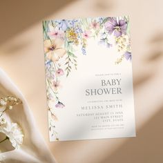 a baby shower card with flowers on it next to a bouquet of white and purple flowers