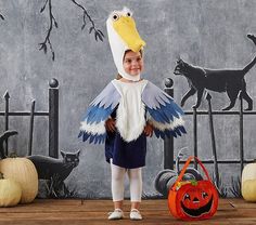 a young child wearing a bird costume standing in front of halloween decorations and pumpkins