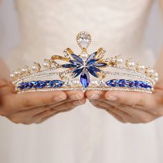 a close up of a person holding a tiara with pearls and blue crystals on it