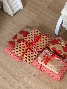 three wrapped presents sitting on the floor with red bows and hearts around them, tied in twine