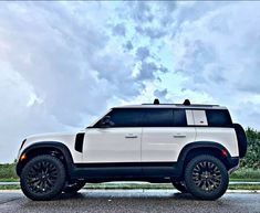 a white and black suv parked on the side of the road with clouds in the background