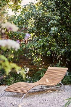 a wooden chaise lounge chair sitting in the middle of a garden