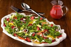 a salad with strawberries, oranges and other vegetables in a white bowl on a wooden table