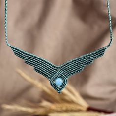 a blue beaded necklace is hanging from a string on a piece of cloth with wheat stalks in the background