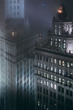 the top of two buildings at night with lights on and fog in the sky behind them