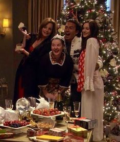 a group of people standing in front of a christmas tree with food on the table