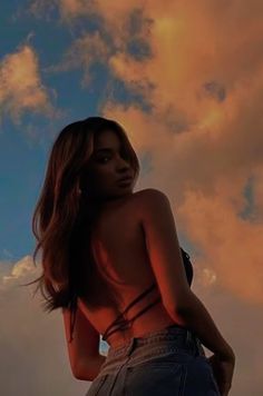 a woman standing in front of a cloudy sky with her back turned to the camera