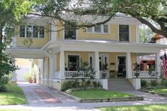 a yellow house with white trim on the front porch