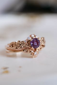 a close up of a ring with a purple stone in the center and diamond accents