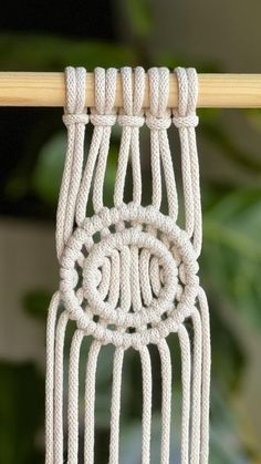 a white macrame hanging on a wooden stick with green leaves in the background