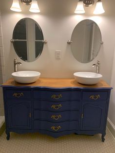 two sinks are on top of a blue dresser in a bathroom with mirrors above them