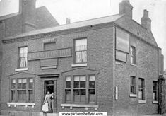 an old black and white photo of a woman standing in front of a brick building