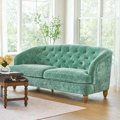 a green couch sitting in front of a window next to a table with flowers on it