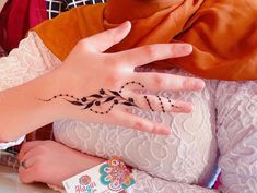 a woman's hand with a henna tattoo on her left wrist and an orange scarf around her neck