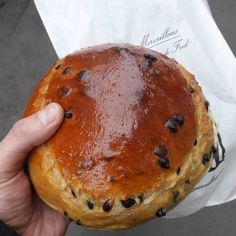 a person holding a pastry with chocolate chips on it in front of a paper bag