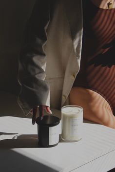 a person holding a candle next to a cup on a table