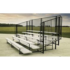 several white benches sitting next to each other in front of a metal fence and grassy field