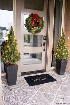 two potted christmas trees sitting in front of a welcome mat on a door way