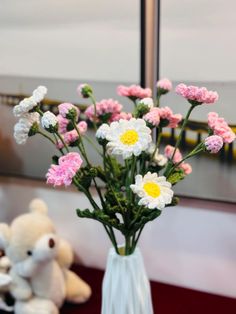 a vase filled with pink and white flowers next to a teddy bear